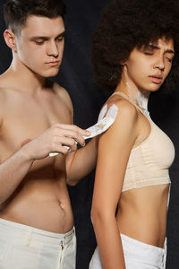 Man applying paint on woman while standing against black background