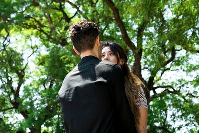 Low angle view of romantic couple standing against trees at park