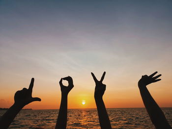 Silhouette cropped hands gesturing by sea against sky at sunset
