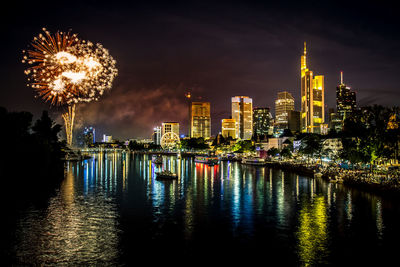 Firework display over river and illuminated buildings in city