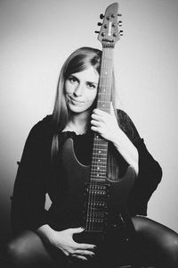 Portrait of young woman holding electric guitar while sitting against white background