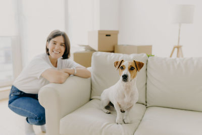 Portrait of woman with dog crouching by sofa at home