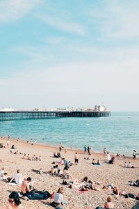 People at beach by pier against sky