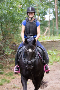 Smiling woman riding horse on field at forest