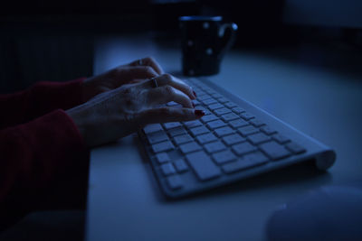 Cropped hands of woman using computer keyboard on table in darkroom at home