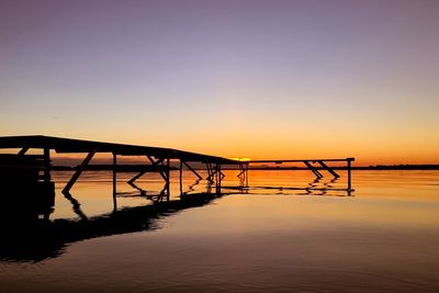 Silhouette pier over sea against clear sky during sunset