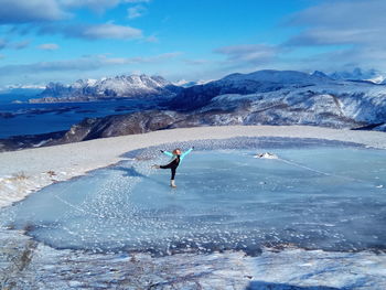 Woman standing on frozen lake by snowcapped mountains during winter