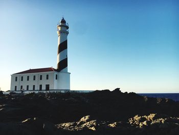 Lighthouse by sea against buildings against clear sky
