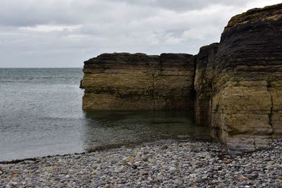 Scenic view of cliffs and sea with pebble beach against sky 