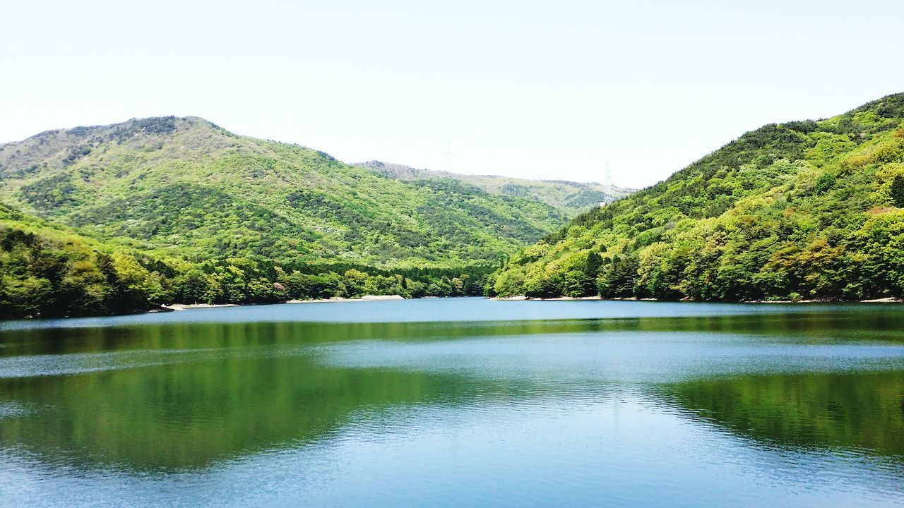 water, mountain, tranquil scene, tranquility, tree, waterfront, lake, scenics, clear sky, reflection, beauty in nature, nature, idyllic, mountain range, river, green color, non-urban scene, day, calm, sky