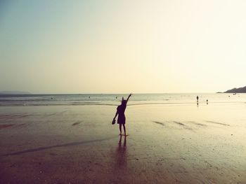 Rear view of woman showing peace sign at beach against clear sky