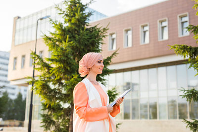 Woman holding umbrella while standing by building