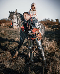 Woman sitting on horse with warrior standing on field