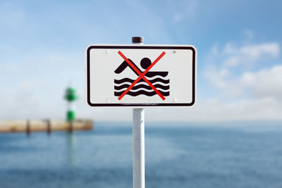 Close-up of road sign by sea against sky