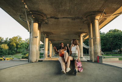 Cheerful teenage girls with basketball and skateboard enjoying under bridge