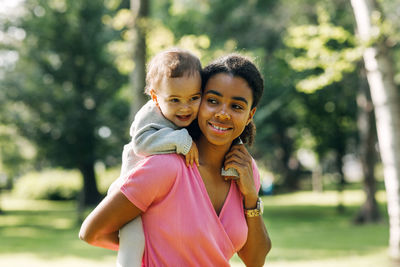 Smiling mother carrying baby girl on back in park