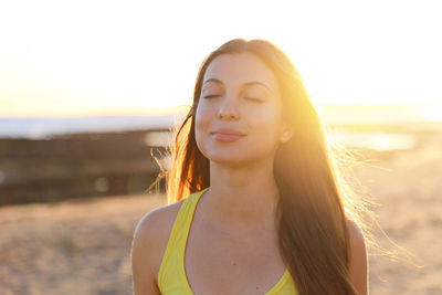 Smiling young woman with eyes closed while standing at beach