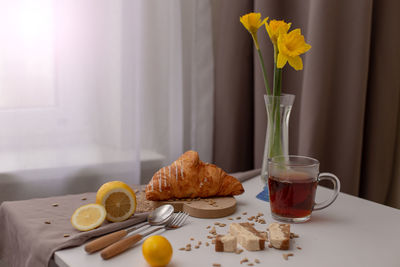 Breakfast with a cup of tea, croissants, lemons and yellow narcis in a glass vase