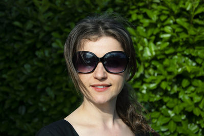 Portrait of woman wearing sunglasses while standing against plants