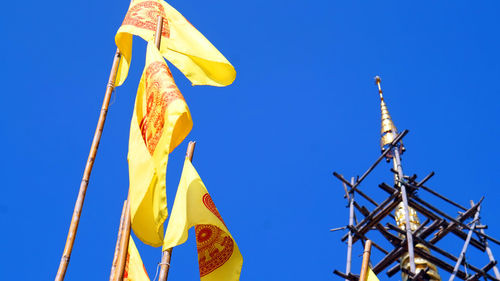 Low angle view of bhuddhist yellow  flags against clear blue sky in temple
