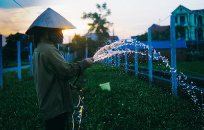 Side view of female farmer spraying water at farm during sunset