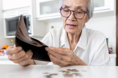 Close-up of senior woman removing coins from wallet on table