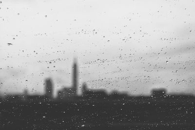 Silhouette buildings and field seen through wet glass window