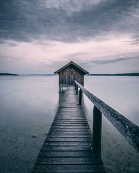 Wooden jetty leading to pier over sea against sky