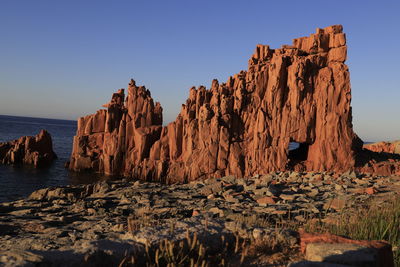 Rock formations by sea against clear blue sky