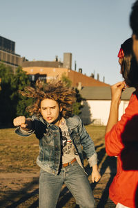 Friend looking at young man gesturing on field during sunny day