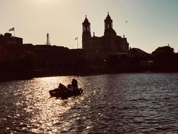 Silhouette people on boat in river against sky