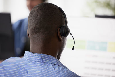 Rear view of man using headset while sitting in office