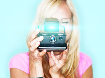 Woman photographing from polaroid camera against colored background