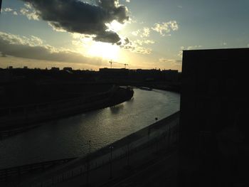 Silhouette cityscape by river against sky during sunset