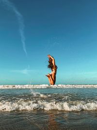 Young woman jumping at beach against sky during sunset