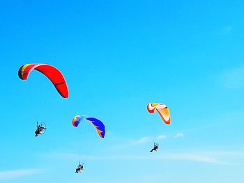 Low angle view of people paragliding against blue sky