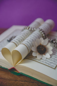 Close-up of koran with prayer beads and flower on table