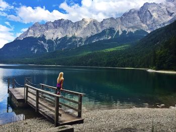 Man standing on railing by lake against mountains