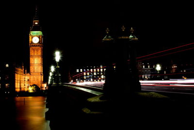 Light trail on bridge against illuminated big ben at night in city