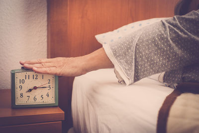 Cropped hand turning off alarm clock in bedroom at home