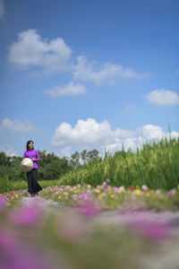 Woman standing on purple flowering plants on field against sky