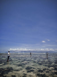 People angling while standing in sea against sky