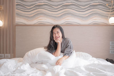 Portrait of smiling woman sitting on bed at home