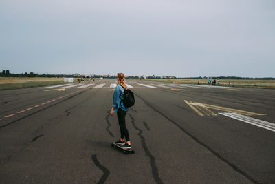 Woman with umbrella on airport runway against sky