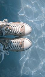 Low section of person wearing canvas shoes over swimming pool