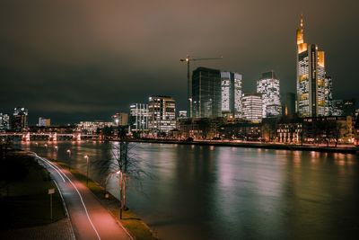 Illuminated buildings by river against sky at night