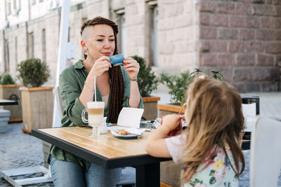 Mother and little daughter eating in the street cafe. trendy hipster mother with dreadlocks and