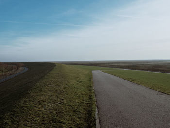 Empty road amidst field against sky