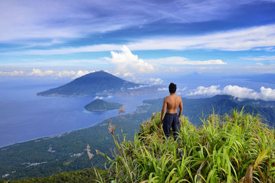 Rear view of shirtless man looking at mountains against sky