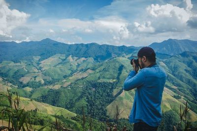 Man photographing mountains against cloudy sky